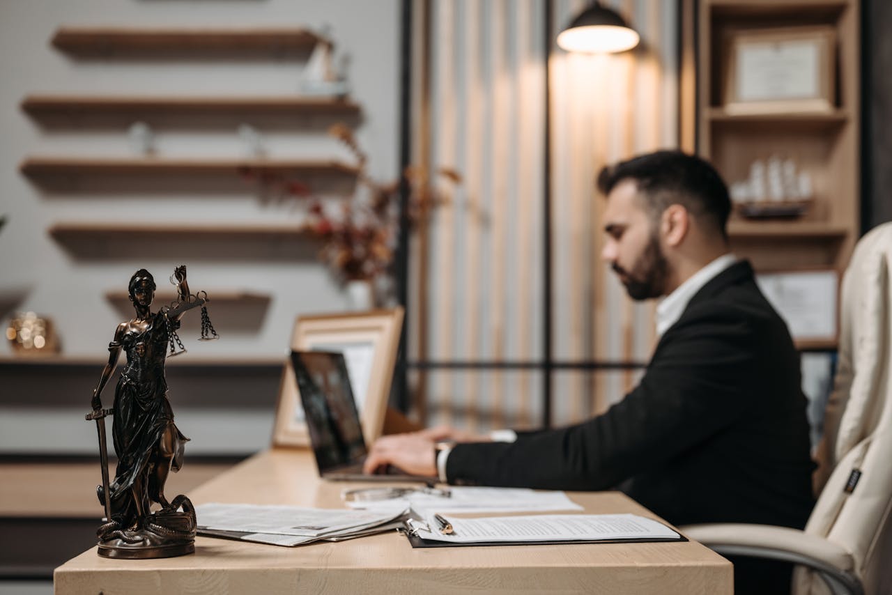 Lawyer working diligently on a laptop in a modern office, Lady Justice statute present.